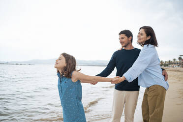 Happy mother and father holding hands with daughter enjoying at beach - JOSEF20054