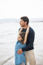 Smiling father and daughter standing at beach - JOSEF20075