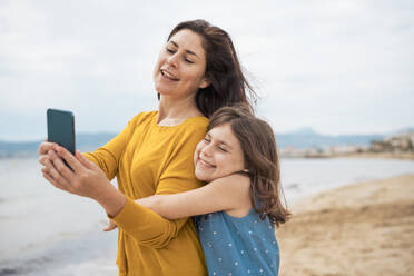 Smiling woman taking selfie through smart phone with daughter at beach - JOSEF20093