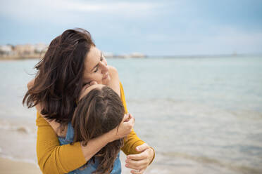 Girl kissing mother on cheeks in front of sea - JOSEF20106