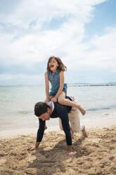 Father giving piggyback ride to daughter on sunny day at beach - JOSEF20132