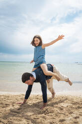 Cheerful girl enjoying piggyback ride in front of sea - JOSEF20134