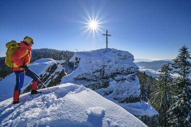 Woman in ski-wear hiking near summit cross on snow covered mountain - ANSF00450