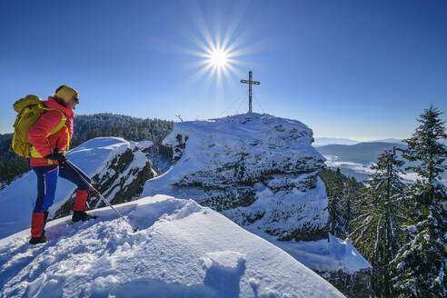 Frau in Skikleidung beim Wandern in der Nähe des Gipfelkreuzes auf einem schneebedeckten Berg - ANSF00450