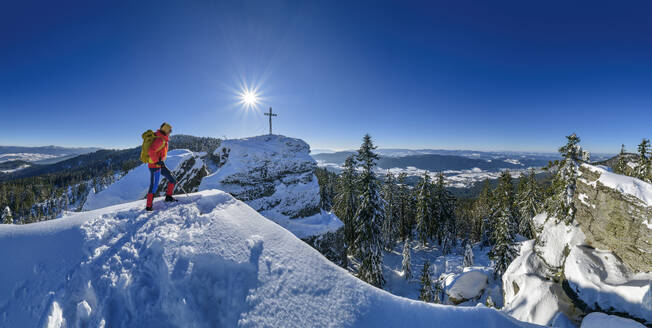 Woman in ski-wear hiking near summit cross on snowcapped mountain - ANSF00451