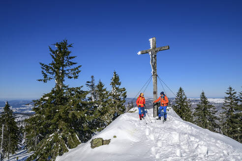 Ski couple standing under crucifixion on snow mountain - ANSF00459