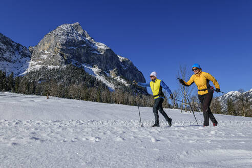 Paar beim Skifahren in schneebedeckter Landschaft am felsigen Berg - ANSF00463