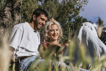 Lächelndes Paar mit Smartphone im Park an einem sonnigen Tag - PBTF00042