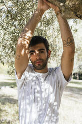 Young man standing under tree on sunny day - PBTF00049