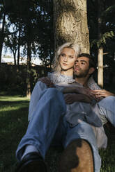 Verliebtes junges Paar sitzt vor einem Baum - PBTF00063