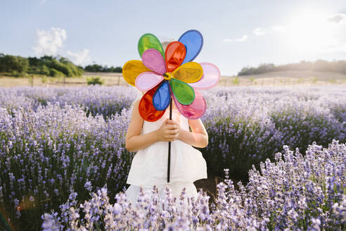 Girl in white dress covering face with pinwheel toy on sunny day - SIF00708
