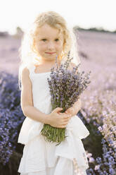 Lächelndes Mädchen hält einen Strauß Lavendelblüten auf einem Feld - SIF00720