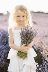 Smiling girl holding bunch of lavender flowers in field - SIF00720