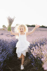 Blond girl holding bunch of lavender flowers running in field - SIF00721