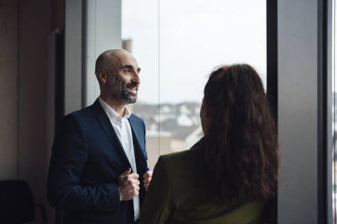 Happy mature businessman talking to colleague in office - JOSEF20138