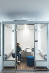 Young businesswoman sitting with laptop inside of office cubicle - JOSEF20147