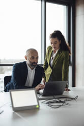 Mature businessman and businesswoman having discussion over laptop - JOSEF20188