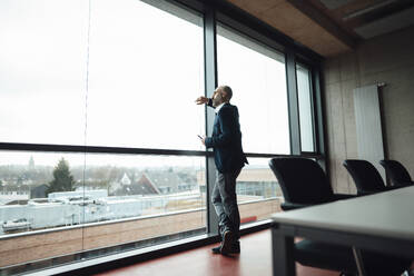 Thoughtful businessman looking through glass window in office - JOSEF20234