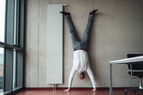 Geschäftsmann übt Handstand vor einer Wand - JOSEF20240