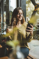 Smiling young woman using mobile phone in cafe - JOSEF20276