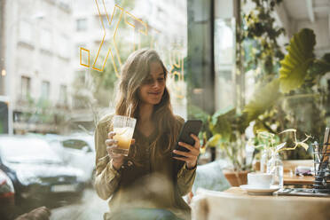 Lächelnde junge Frau mit Saft und Smartphone in einem Café - JOSEF20278