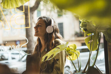 Glückliche Frau mit Kopfhörern, die in einem Café Musik hört - JOSEF20287