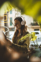 Happy woman wearing headphones listening to music and using tablet PC in cafe - JOSEF20289