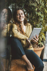 Smiling young woman sitting with tablet PC on seat in cafe - JOSEF20299