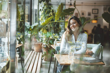 Glückliche junge Frau sitzt am Tisch in einem Café - JOSEF20306