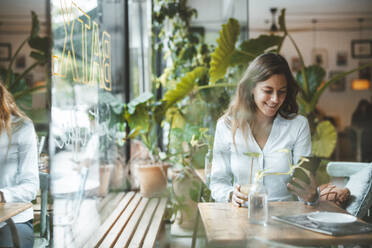 Lächelnde junge Frau, die ein Smartphone am Tisch in einem Café benutzt - JOSEF20307