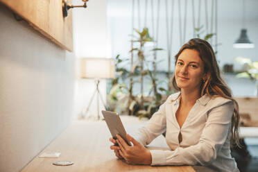 Smiling young businesswoman sitting with tablet PC at desk - JOSEF20323