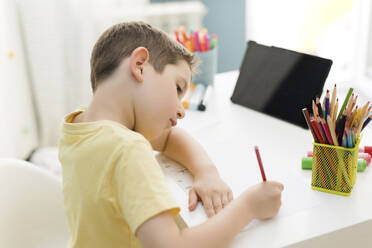 Smiling boy drawing with colored pencil near tablet pc at home - ONAF00586