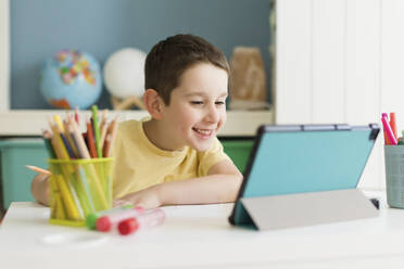 Smiling boy studying on tablet PC at home - ONAF00589
