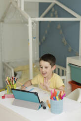 Smiling boy holding colored pencil and talking on video call through tablet PC - ONAF00590