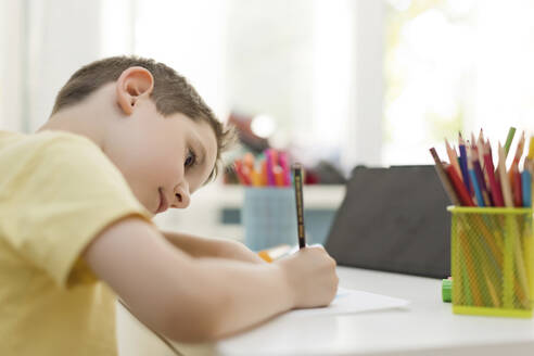 Konzentrierter Junge lernt zu Hause mit Buntstiften zu zeichnen - ONAF00591