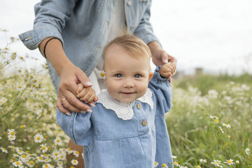 Mother holding smiling daughter's hands at meadow - LESF00376