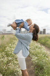 Smiling mother embracing daughter in meadow - LESF00377