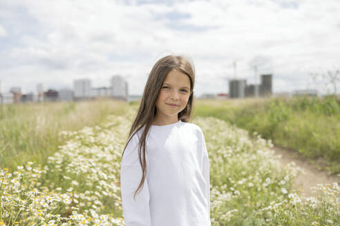 Smiling girl standing in front of daisy plants - LESF00379