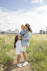 Mother standing with children in meadow on sunny day - LESF00385