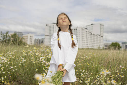 Girl with eyes closed holding bunch of daisy flowers in field - LESF00388