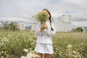 Mädchen versteckt ihr Gesicht mit einem Strauß Gänseblümchen - LESF00389