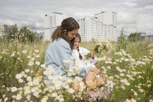 Mother with daughter holding bunch of daisy flowers at meadow - LESF00391