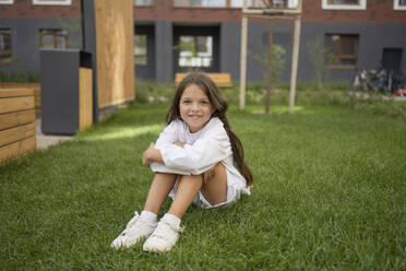 Smiling girl sitting on grass in back yard - LESF00397