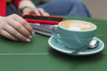 Frau mit Kaffeetasse und Smartphone am Tisch - OSF01914