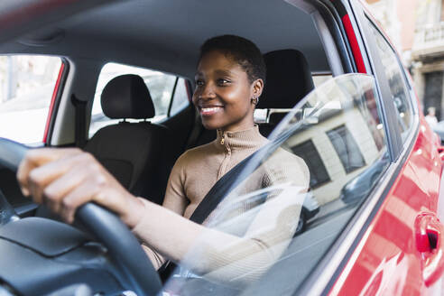 Happy woman holding steering wheel driving red car - PNAF05766