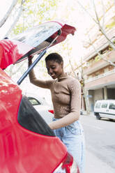 Happy young woman looking in car trunk - PNAF05769