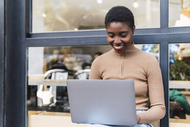 Happy young woman using laptop outside cafe - PNAF05782