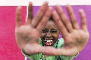 Fröhliche junge Frau mit Stopp-Geste vor einer bunten Wand - PNAF05795