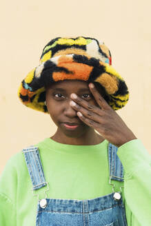 Junge Frau trägt einen bunten Hut und berührt ihr Gesicht - PNAF05810