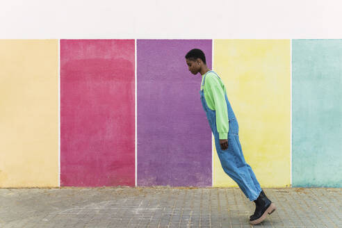 Young woman leaning on tiptoes in front of multi colored wall - PNAF05816